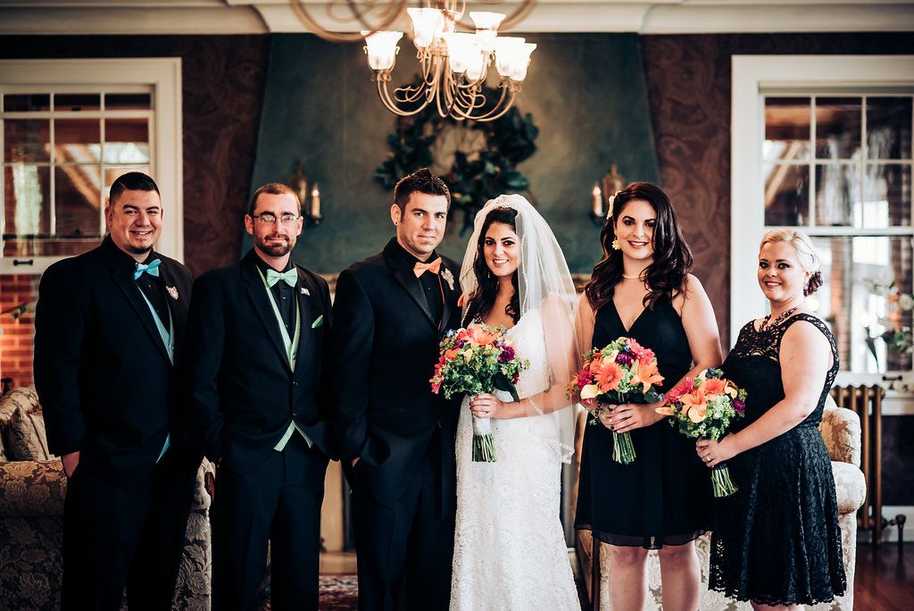 Wedding party poses together in formal attire against elegant interior backdrop with chandelier.