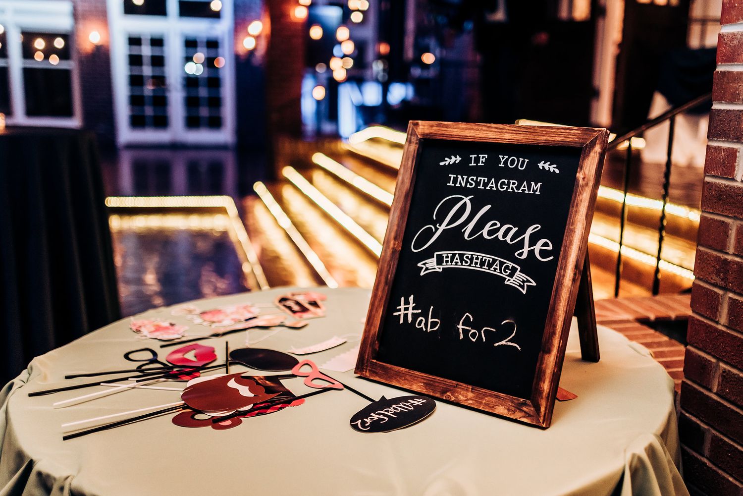 A decorative chalkboard sign with rose petals on a white table at an event.