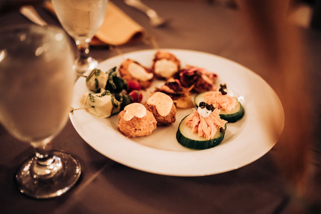 Elegant appetizers and cocktails served on a white plate with mood lighting at an upscale event.