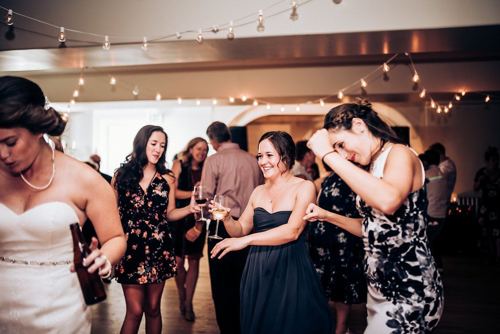 Group of party guests dancing and celebrating in formal attire under string lights.