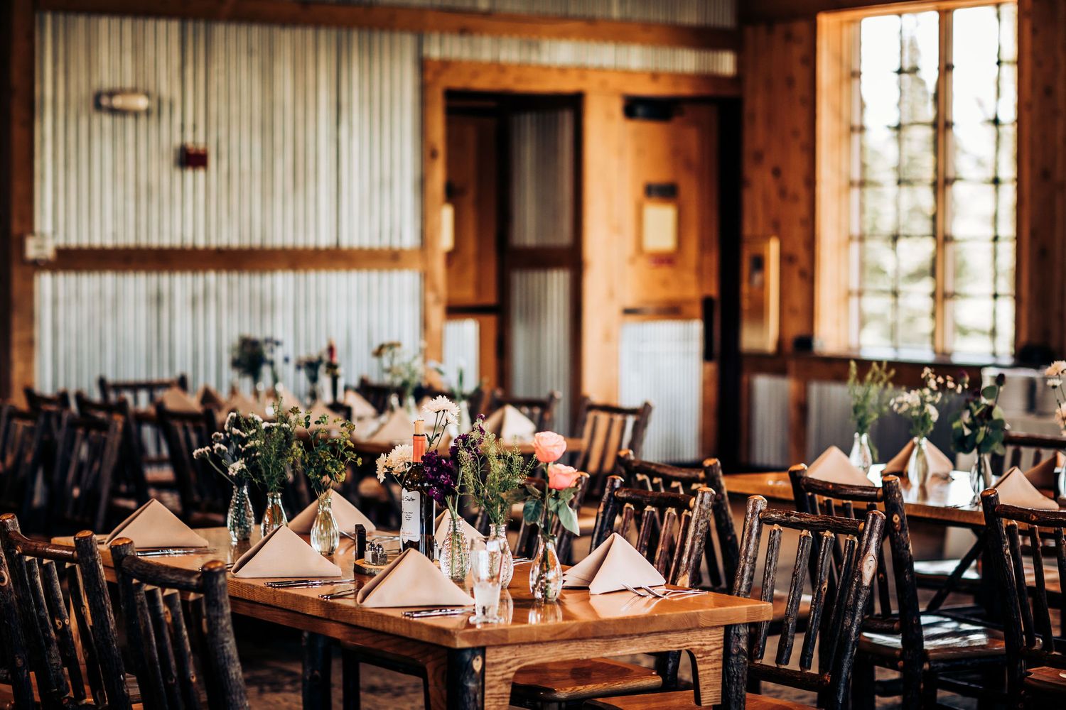 Rustic restaurant interior with wooden tables and chairs set for dining in warm lighting.