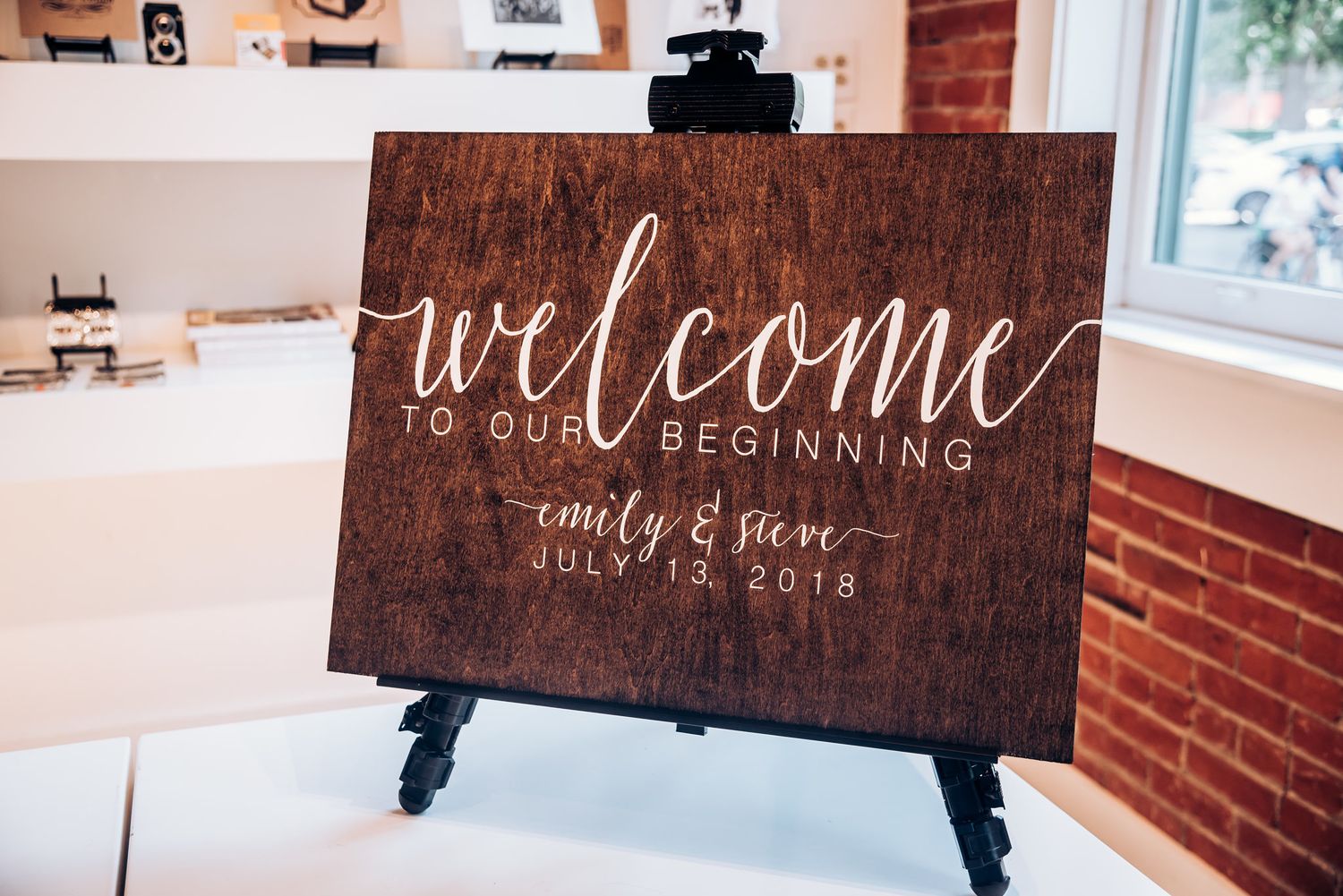 Wooden welcome sign with calligraphy displayed on easel at wedding reception.