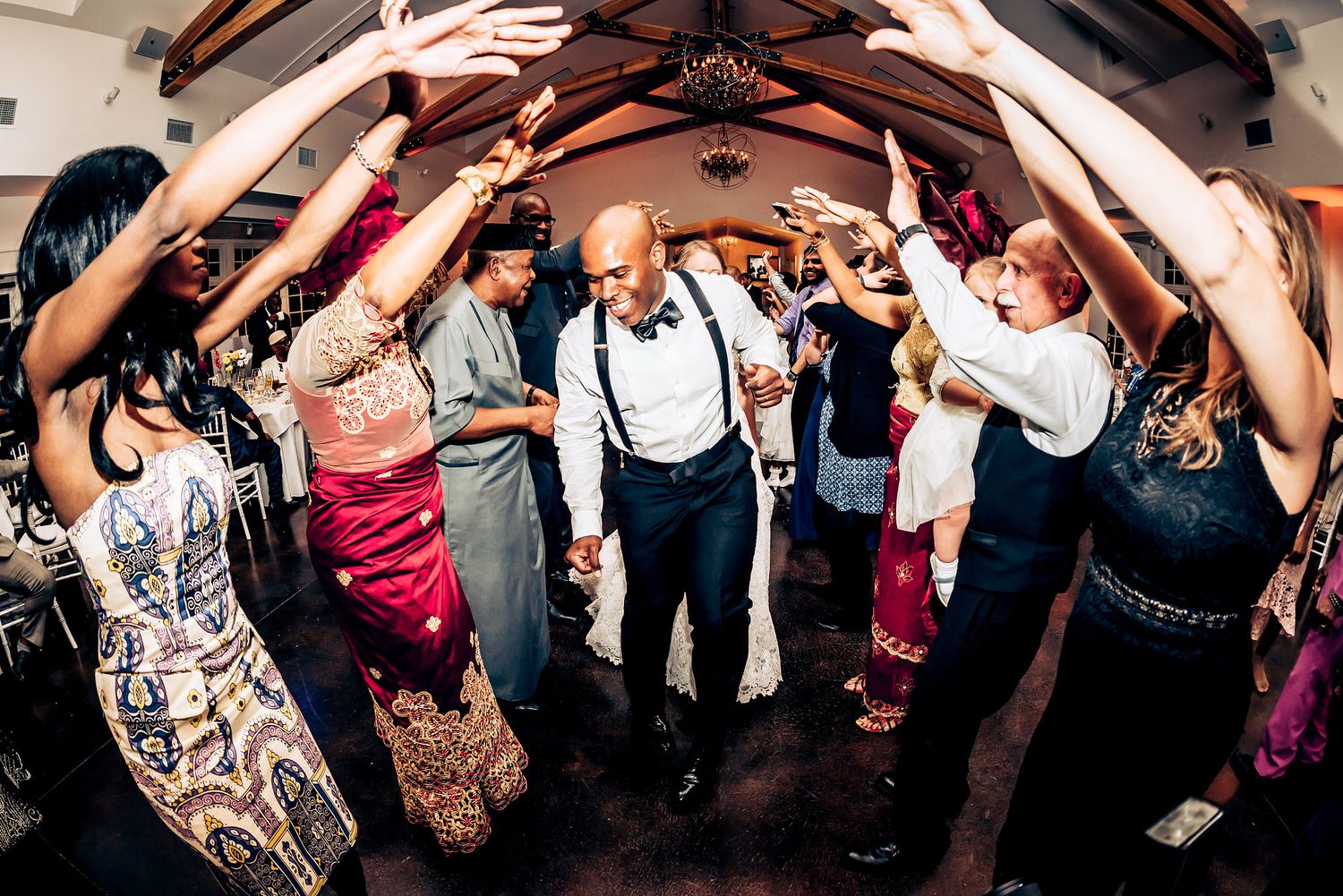 Wedding guests form a dance tunnel with raised arms at the reception.
