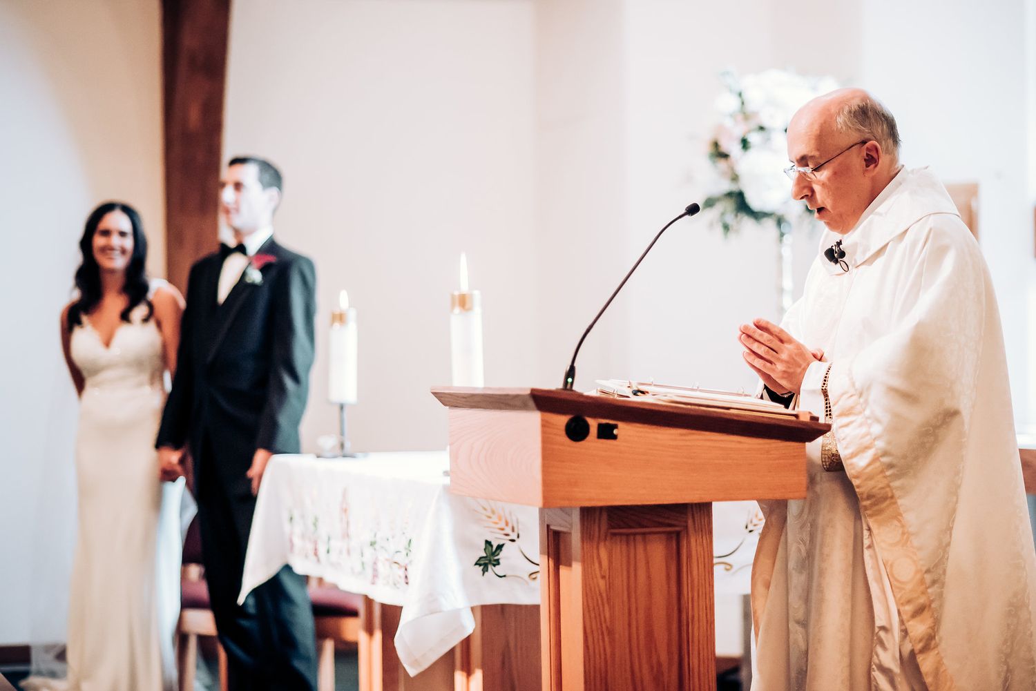 A priest delivers a sermon at the wooden podium during a church wedding ceremony.