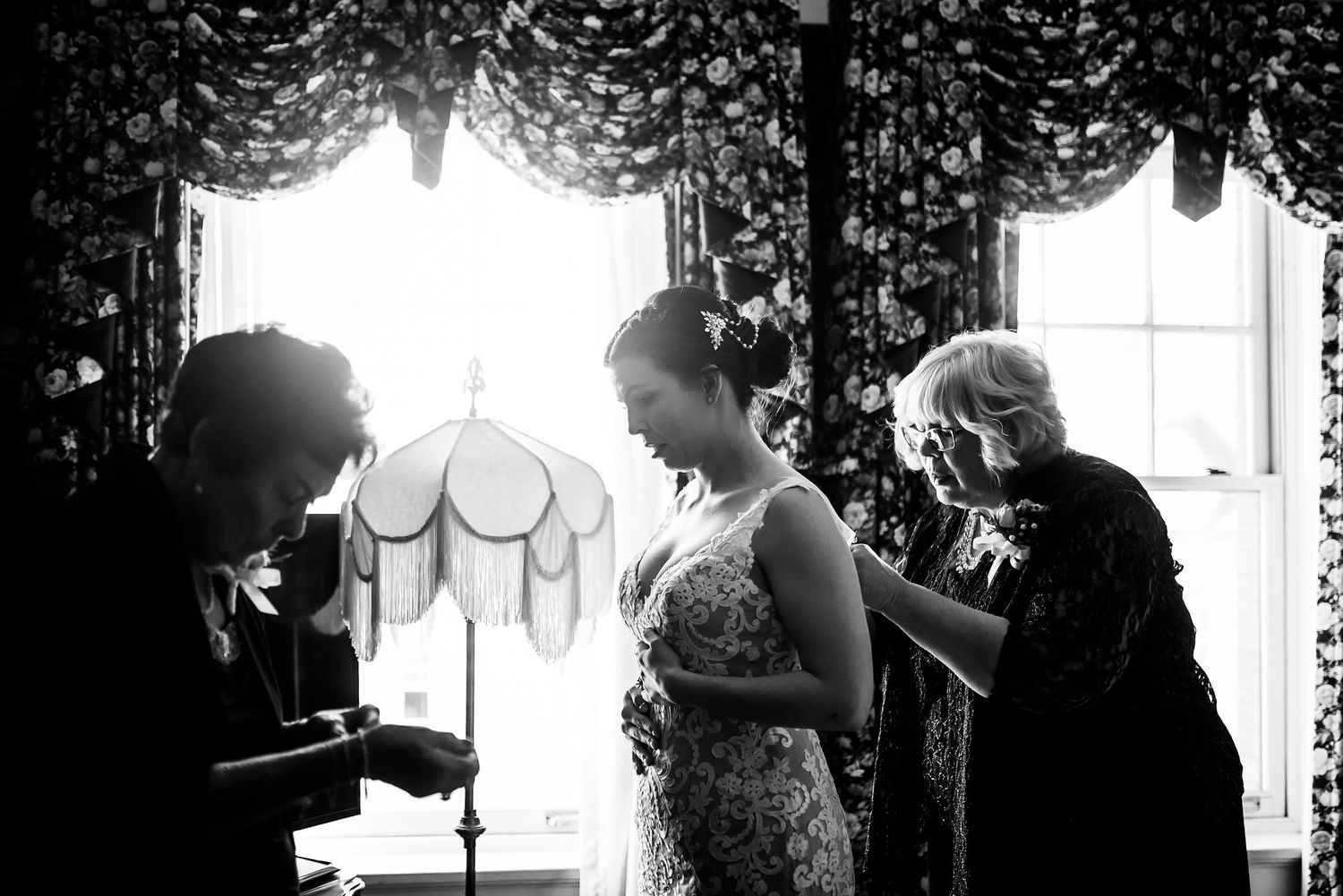 A black and white image showing wedding preparation scene with dramatic window lighting.