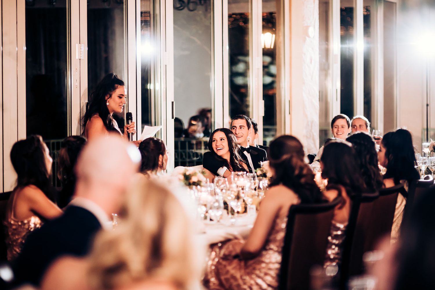 Wedding reception guests gathered around elegantly set dining tables during evening celebration.