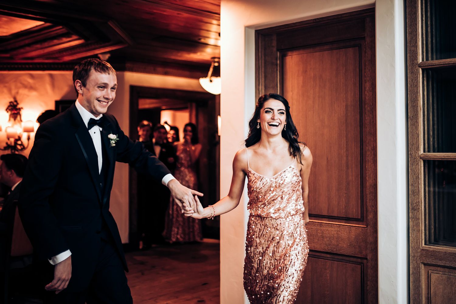 Couple in formal attire entering a warmly lit reception space together.