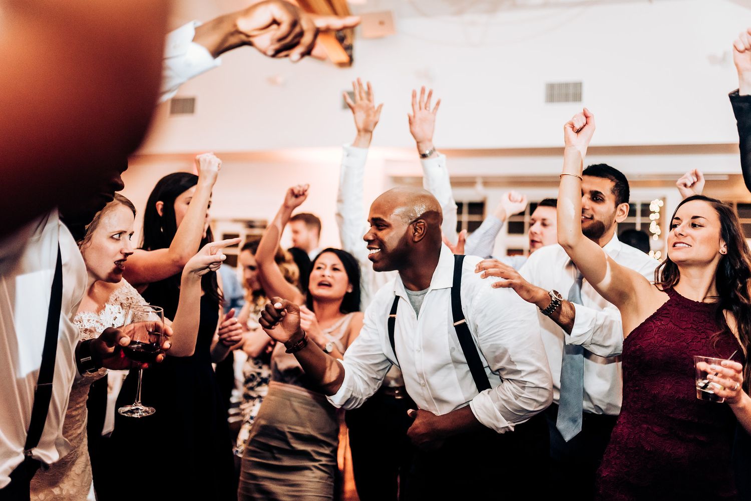Wedding guests dancing and celebrating with raised hands during a lively reception party.