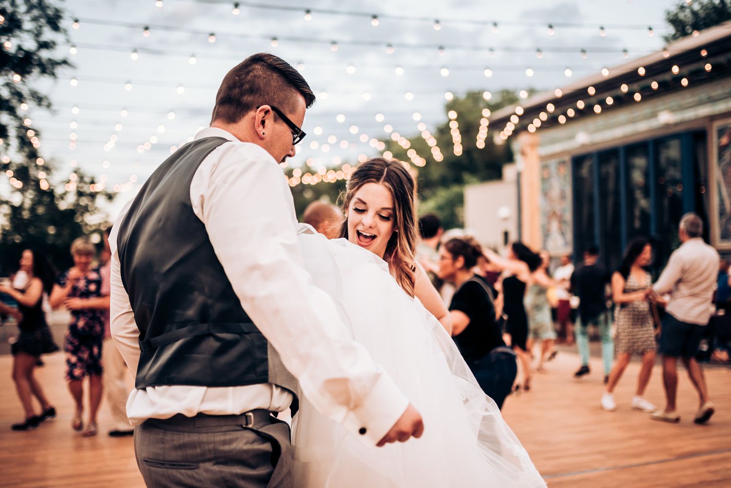 A couple dancing together on an outdoor dance floor beneath twinkling lights.