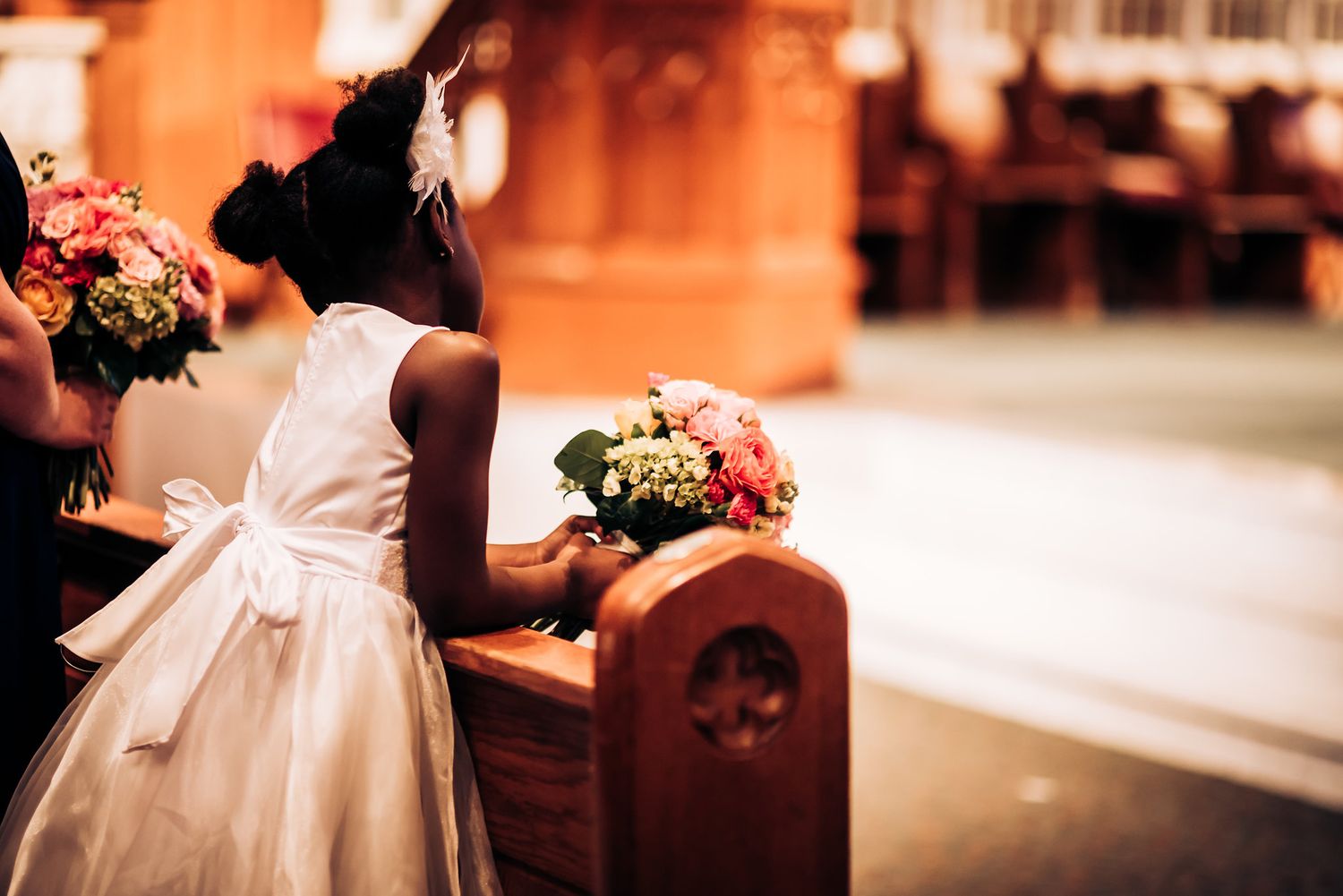 Small flower girls in white dresses kneel at church pews during a wedding ceremony.