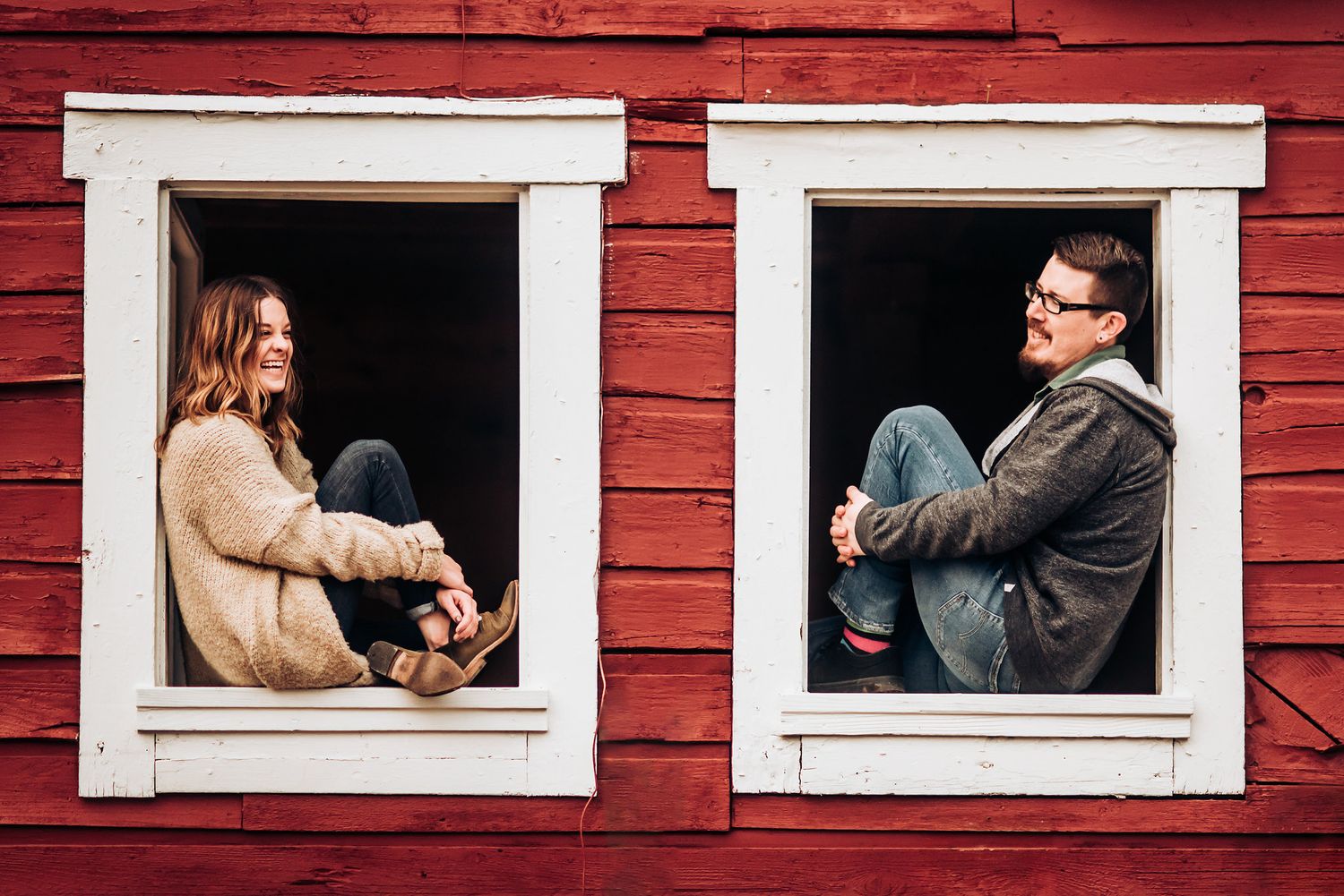 A creative portrait through white window frames of a couple sitting separately in a rustic red building.