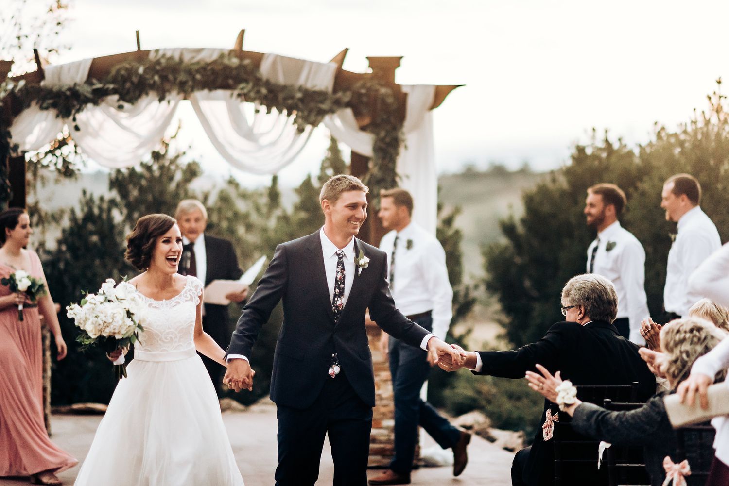 Celebratory moment during outdoor wedding with guests applauding under decorated wooden arch.