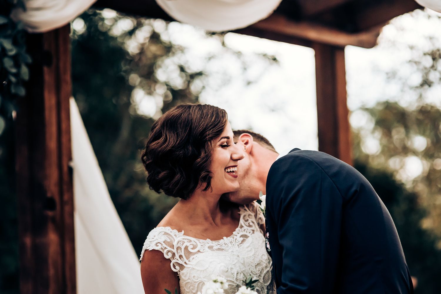 Intimate wedding ceremony moment under draped gazebo with floral decor.