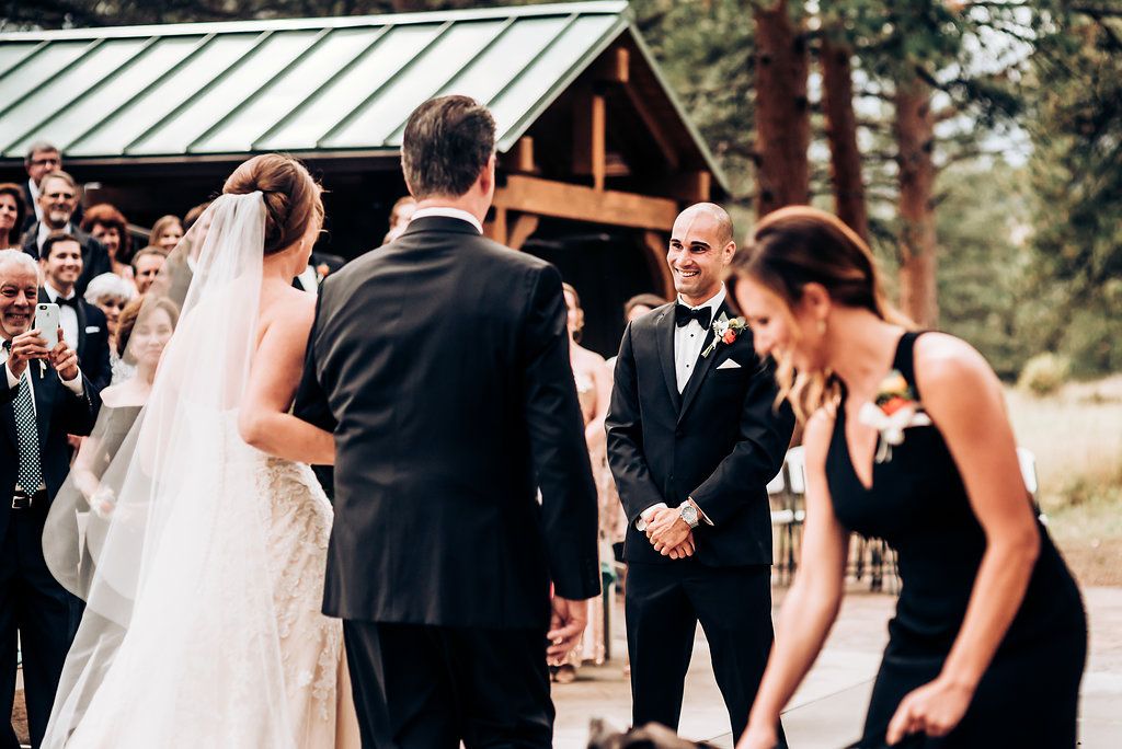Outdoor wedding ceremony under wooden pavilion with guests in formal attire.