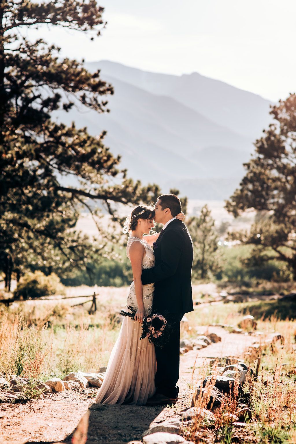 Elegant wedding couple stands on mountain trail with stunning valley views.