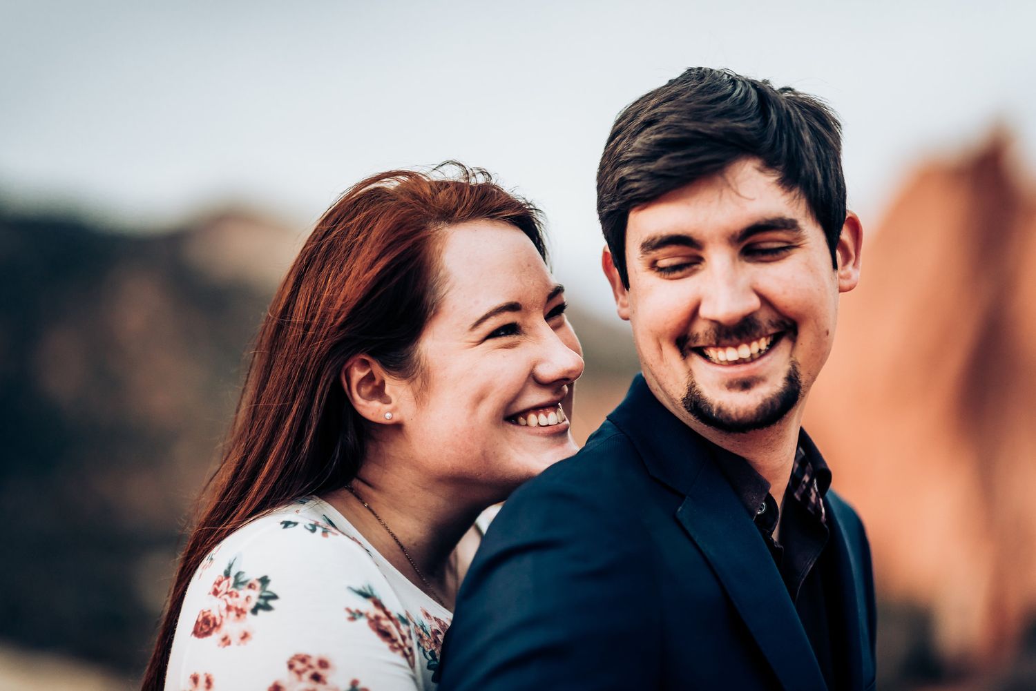 Joyful couple sharing intimate moment against red rock formations during sunset photoshoot.