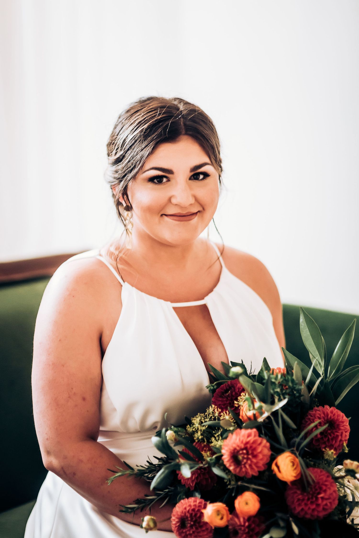 Bridal portrait featuring a stunning coral and burgundy dahlia bouquet against emerald velvet seating.