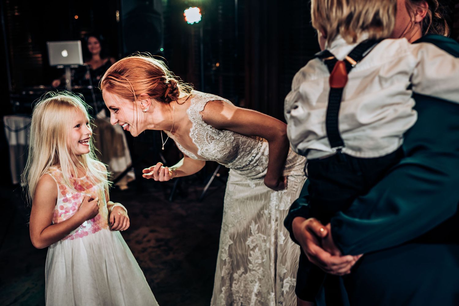 Sweet moment between bride in sparkly gown and young flower girl in white dress during reception.