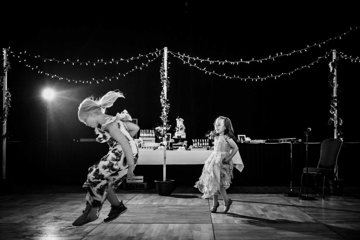 Black and white photo of dancing at wedding reception under string lights.