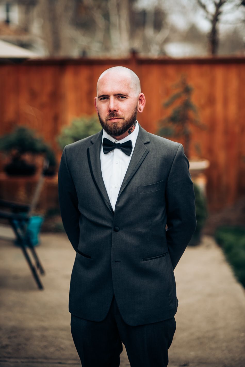 Formal portrait of groom in black tuxedo and bowtie against wooden fence.