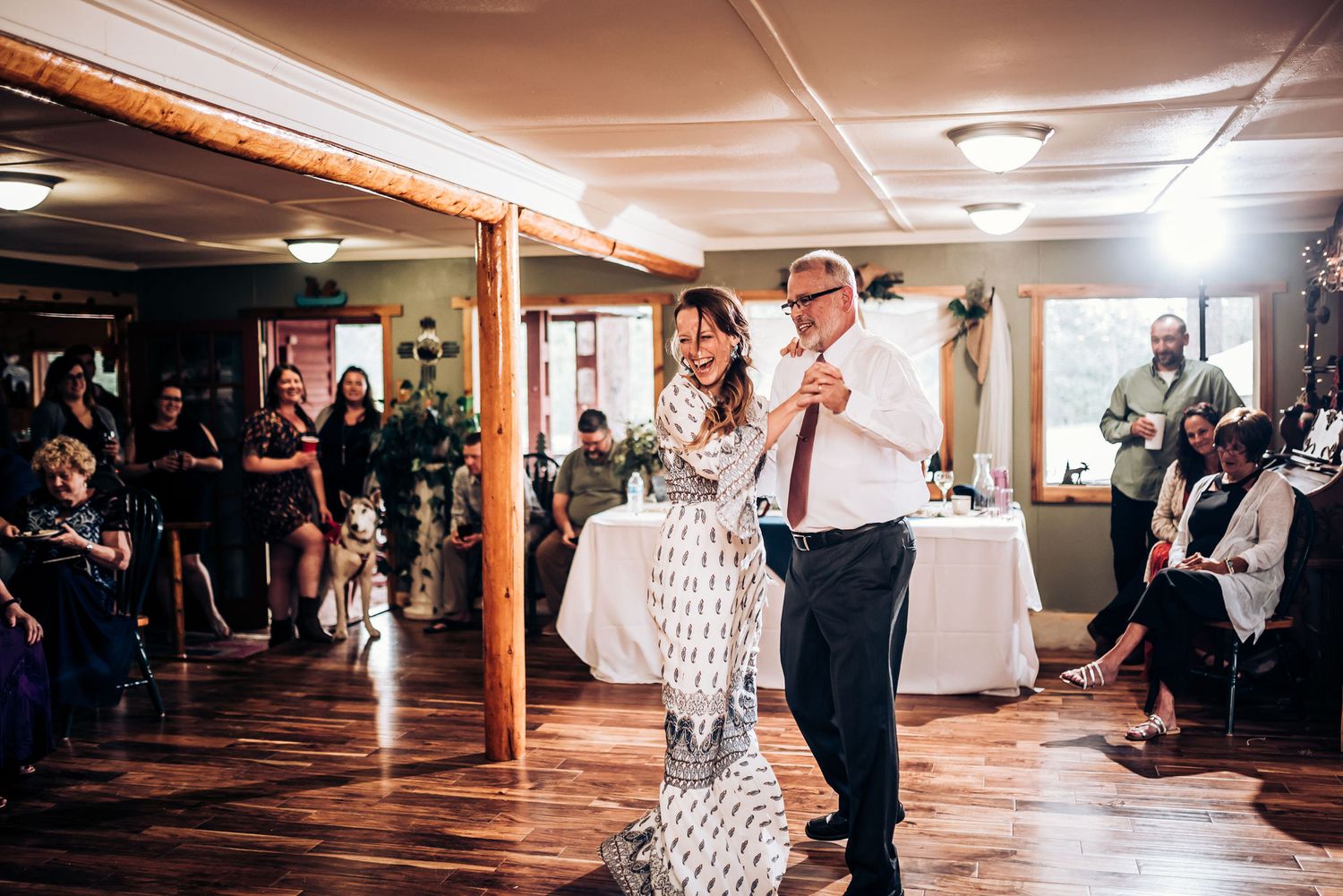 Wedding guests dance energetically on a wooden floor at an indoor reception venue.