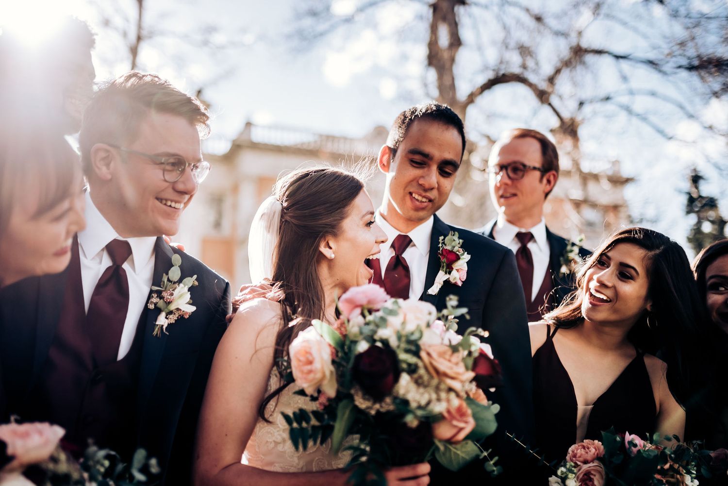 Candid moment of wedding party laughing together outdoors on a sunny day.