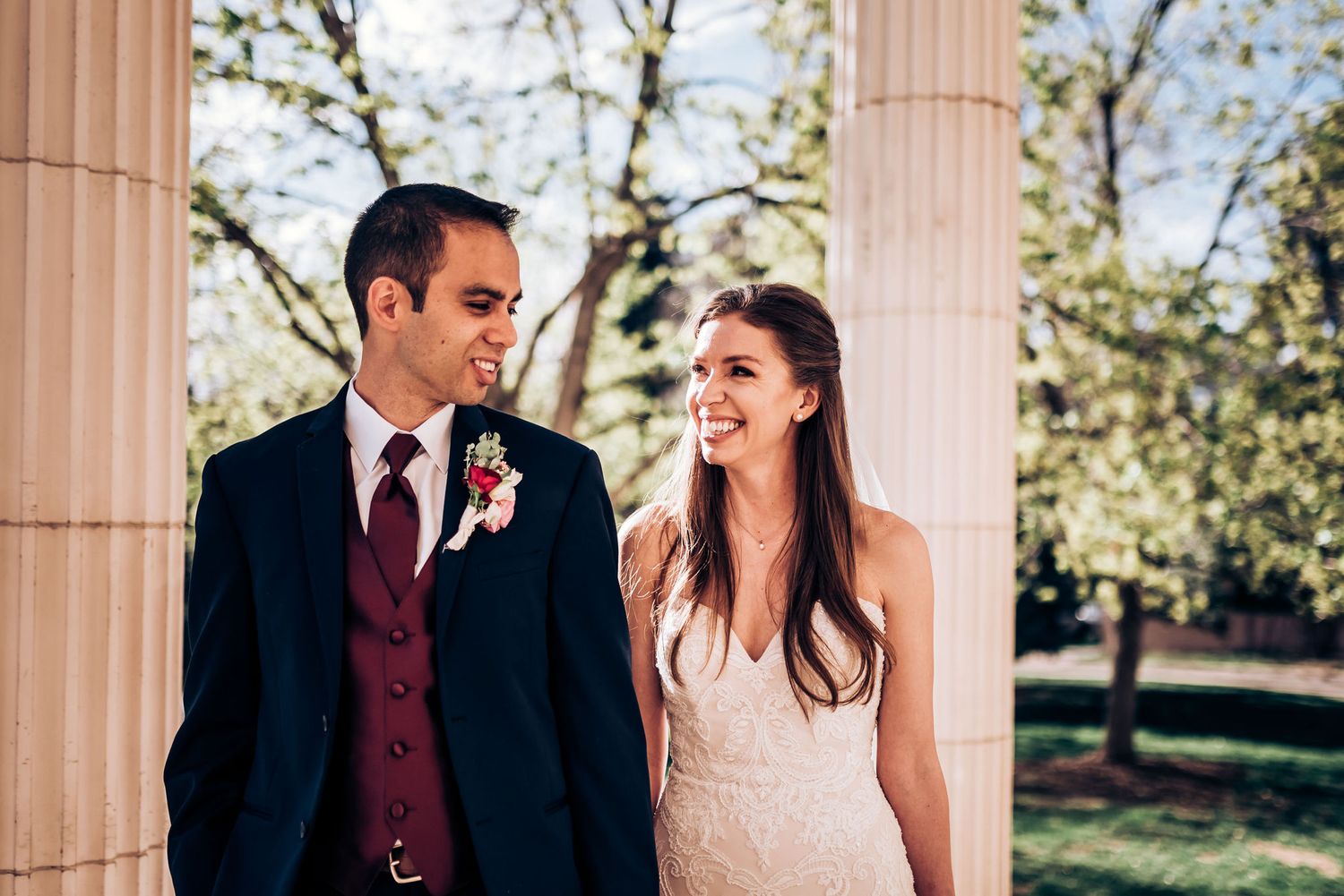 Wedding couple laughs together while standing between classic stone columns.