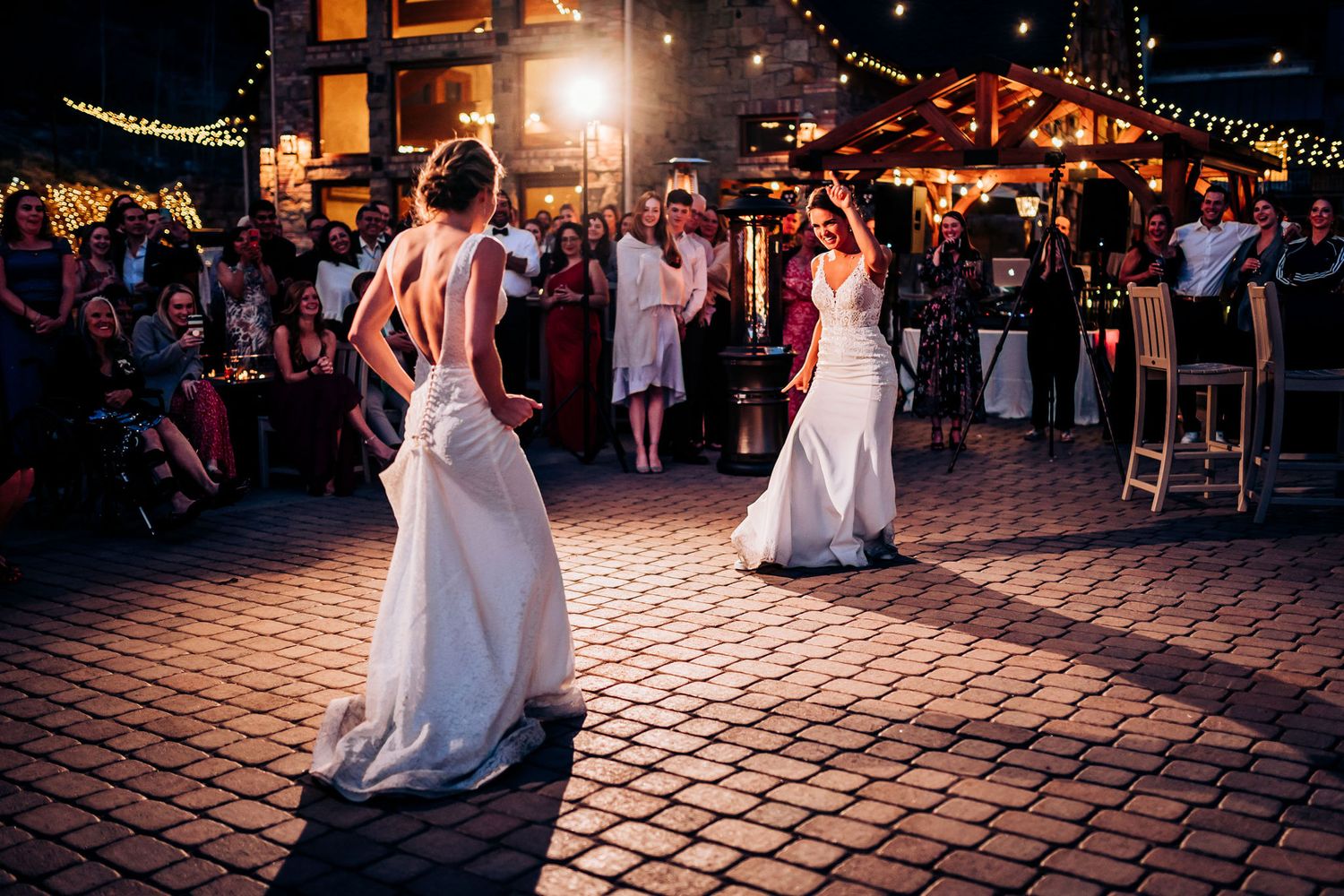 Two dancers in white dresses performing on a brick patio under romantic evening lighting.
