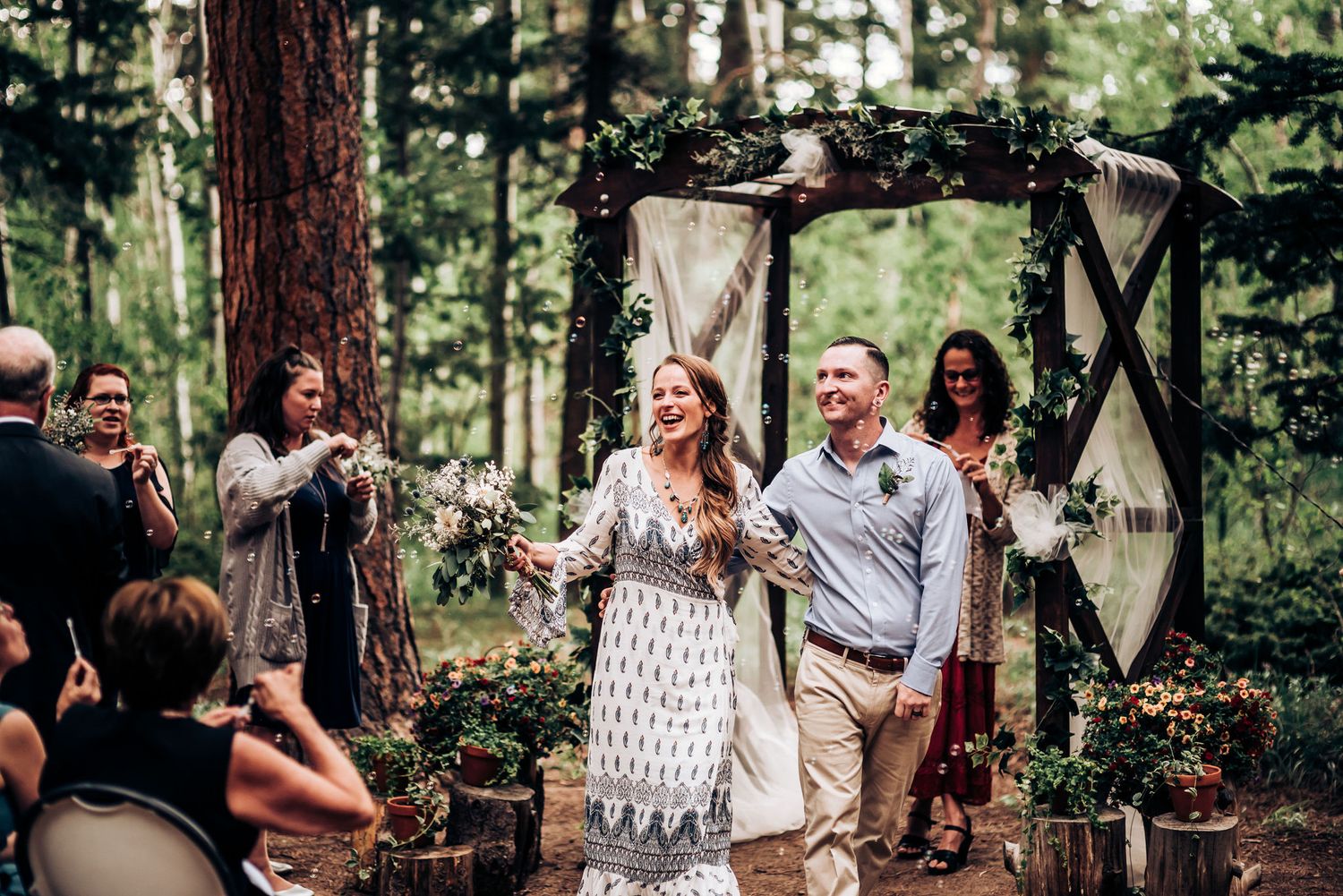 Newlyweds celebrating their first moments as a married couple under a decorated forest arch.