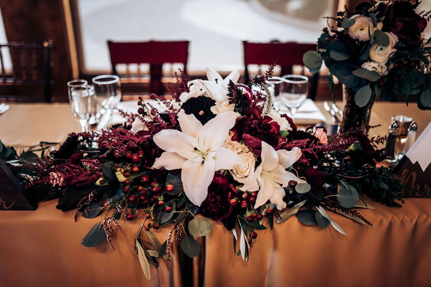 Stunning floral centerpiece with white lilies and burgundy blooms on reception table.