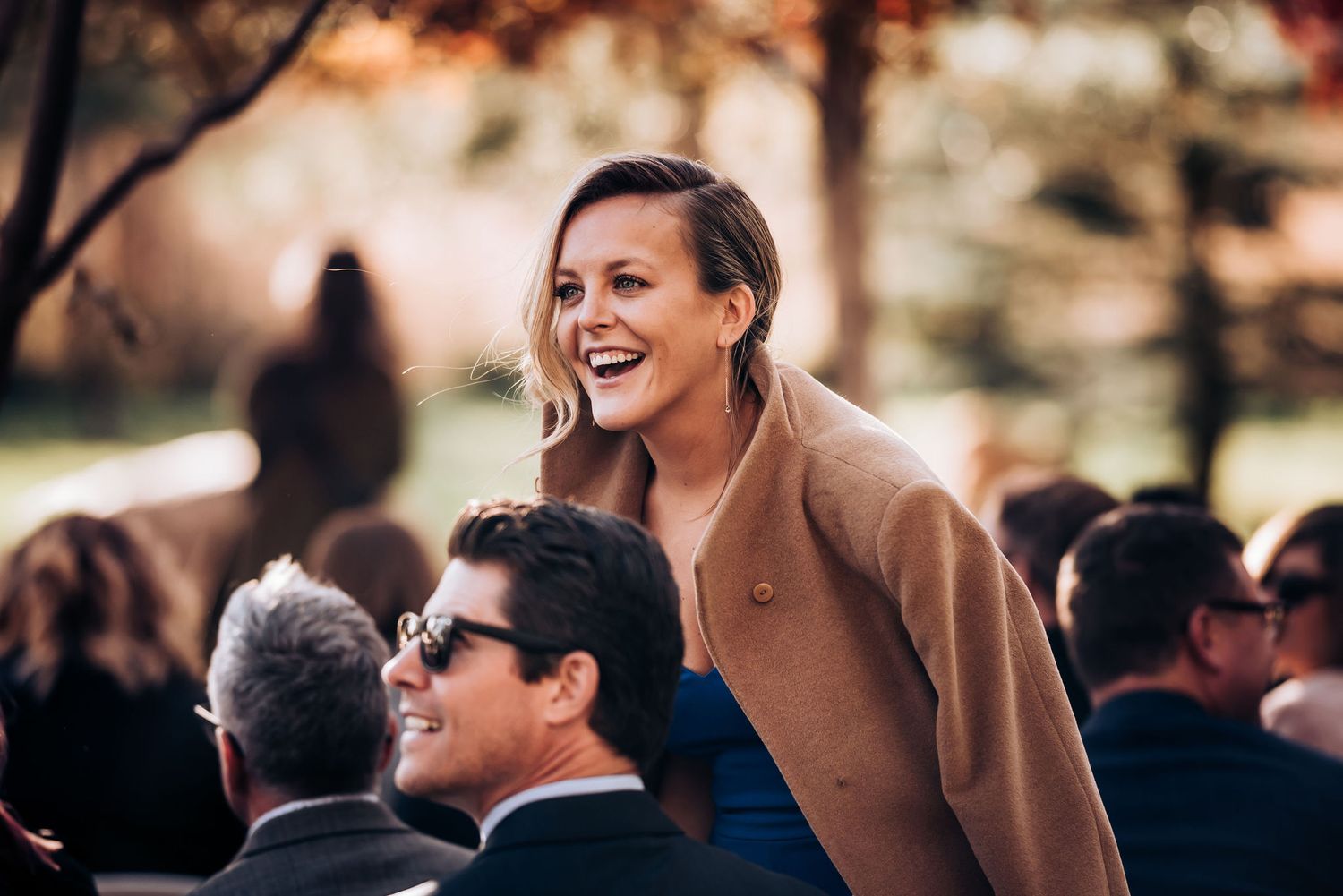 Guests enjoying an outdoor wedding ceremony among autumn trees.