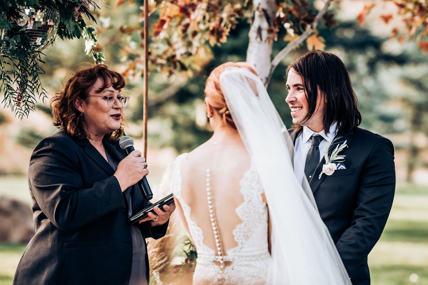 An intimate outdoor wedding ceremony moment with guests watching under autumn trees.
