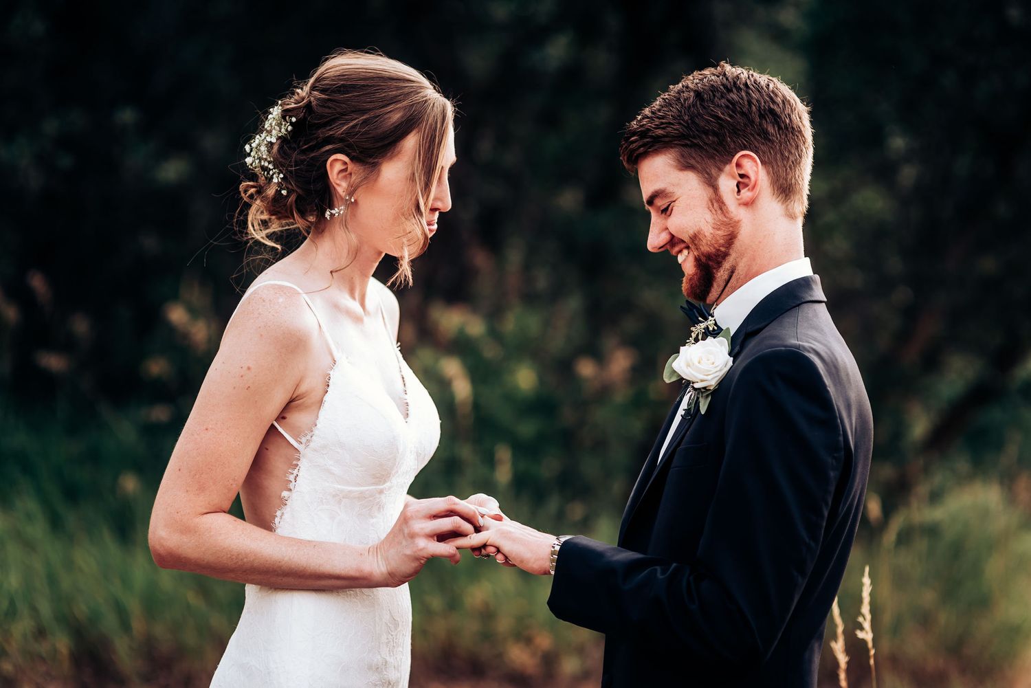 Candid moment of wedding couple during ring exchange in natural outdoor setting.