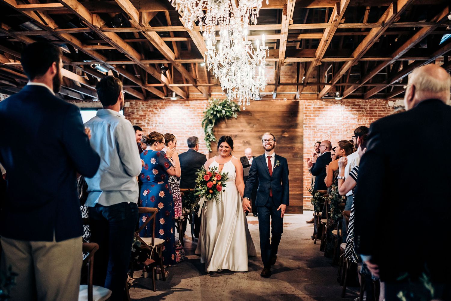 Wedding ceremony procession in urban venue with string lights and wooden details.