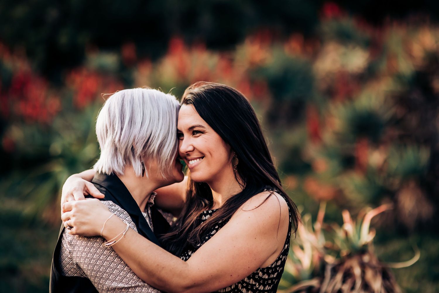 Two people sharing a joyful embrace surrounded by tropical plants and flowers.