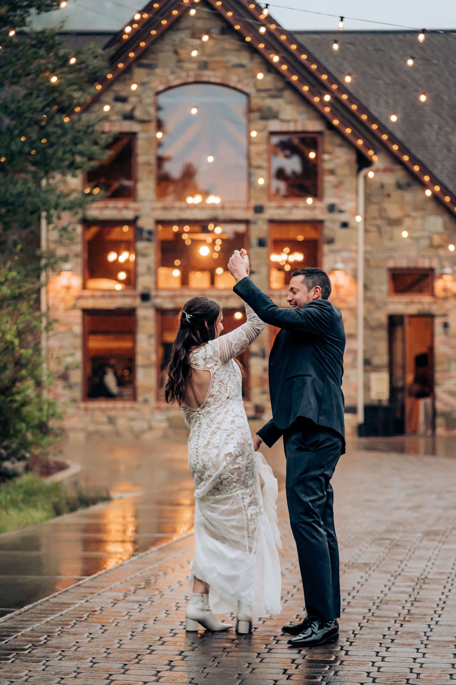 Dancing couple in wedding attire in front of illuminated stone lodge.