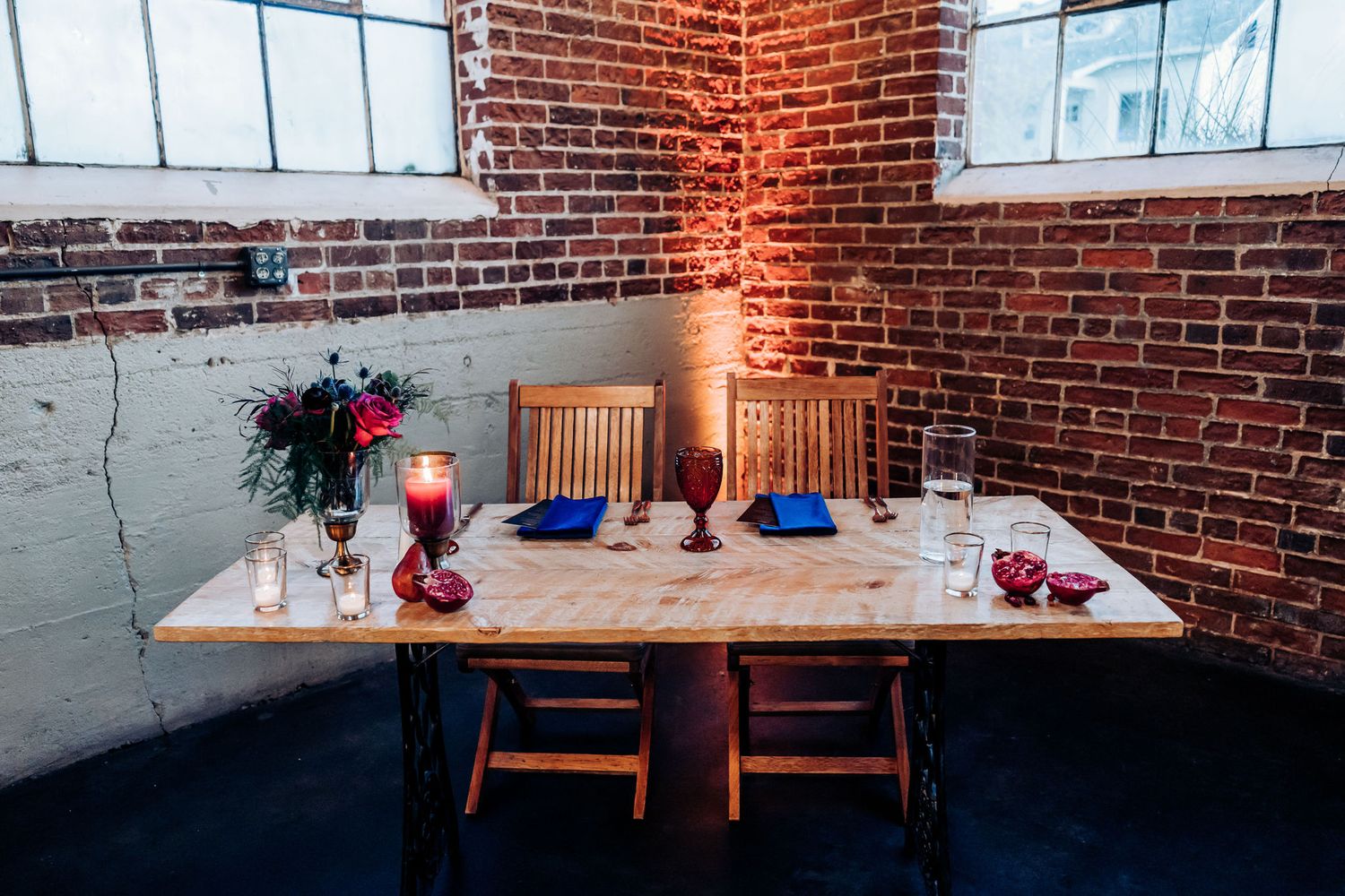 Intimate wedding reception table setup with wooden chairs and red accents against exposed brick wall.