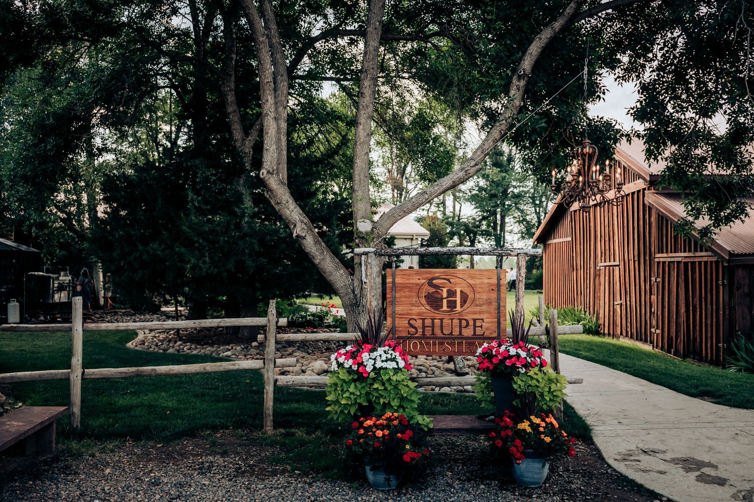 Rustic wedding venue with wooden barn and decorative floral planters along fence path.