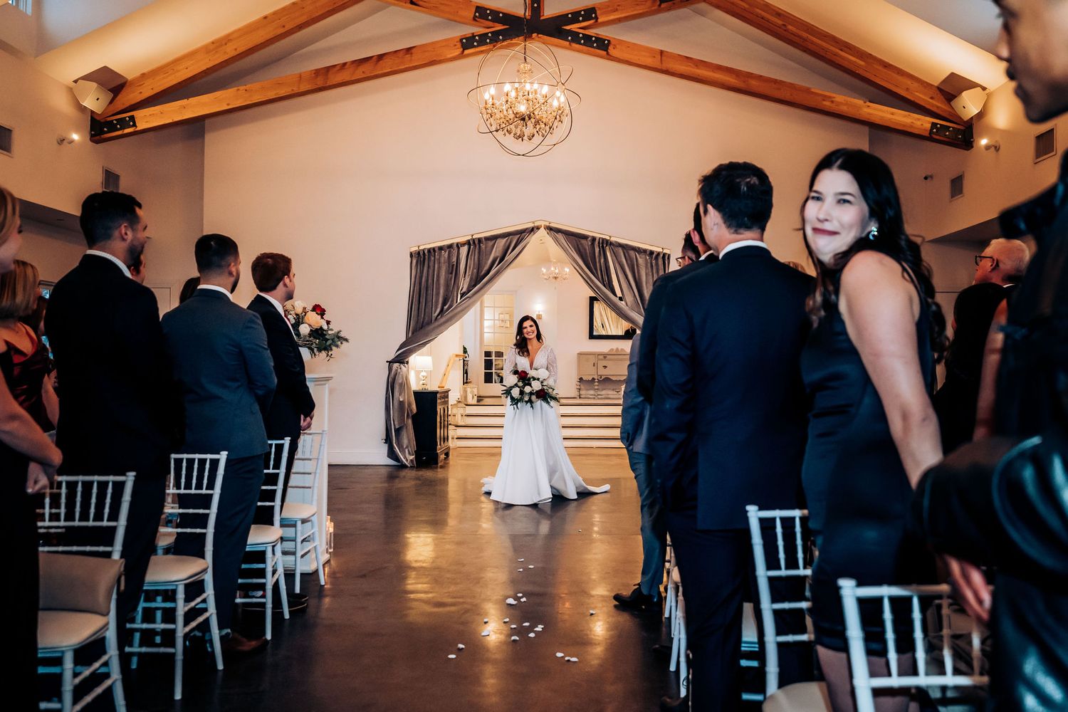 Wedding ceremony in progress inside an elegant venue with wooden beams and formal decor.