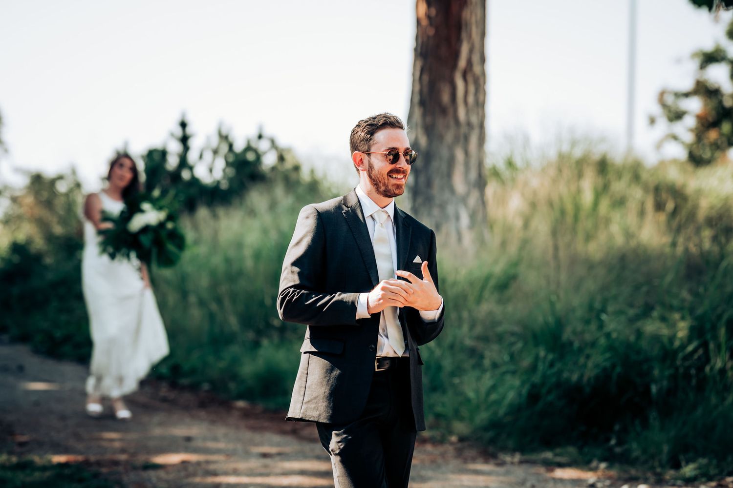 Well-dressed person checking phone outdoors with figure in white dress in background.