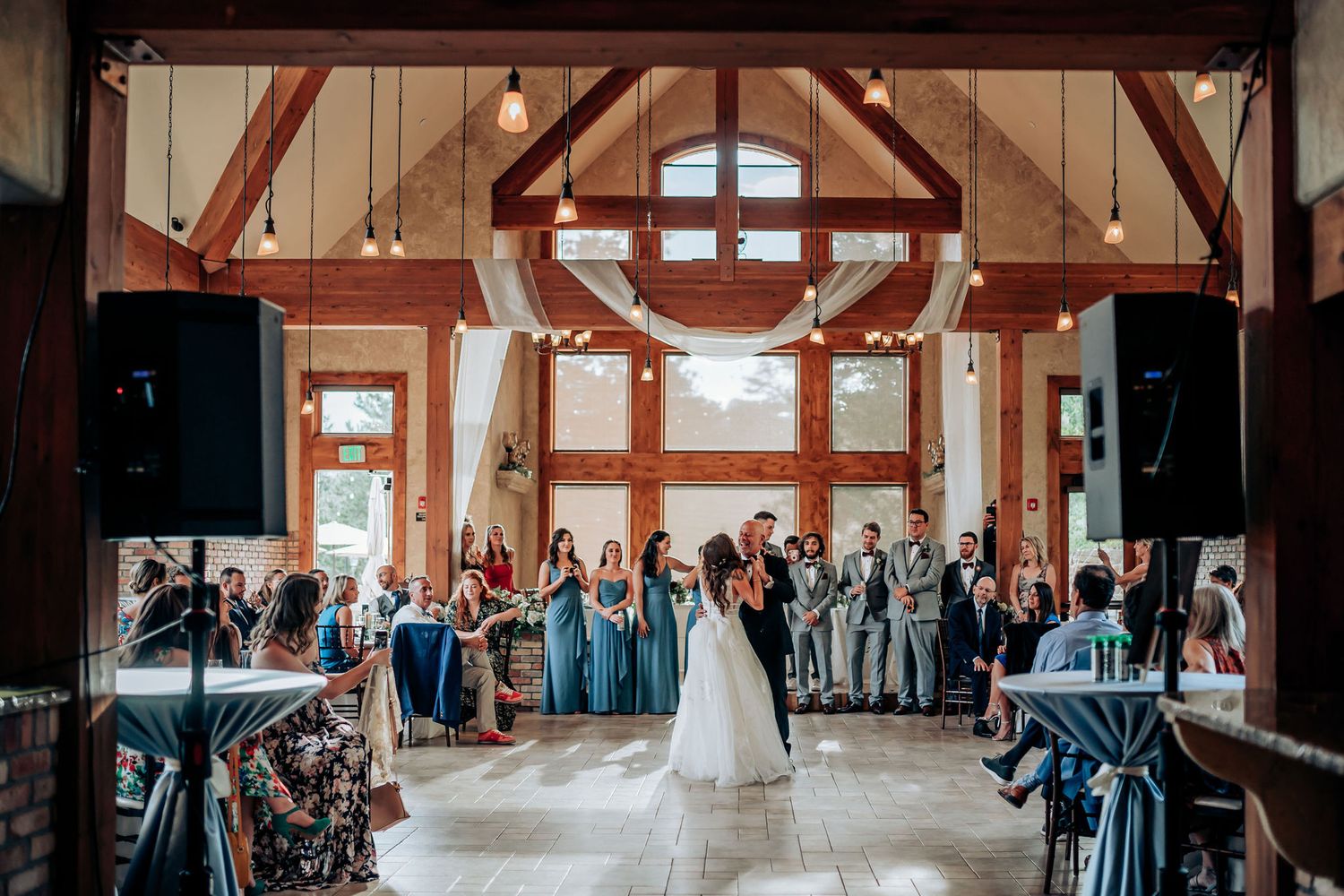 Wedding guests gather in a rustic barn venue with exposed wooden beams and elegant lighting.