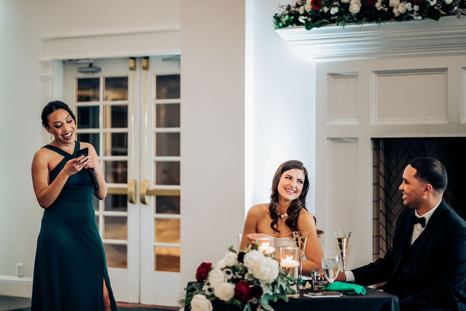Guest delivering speech during wedding reception at elegant venue with white decor and fireplace.