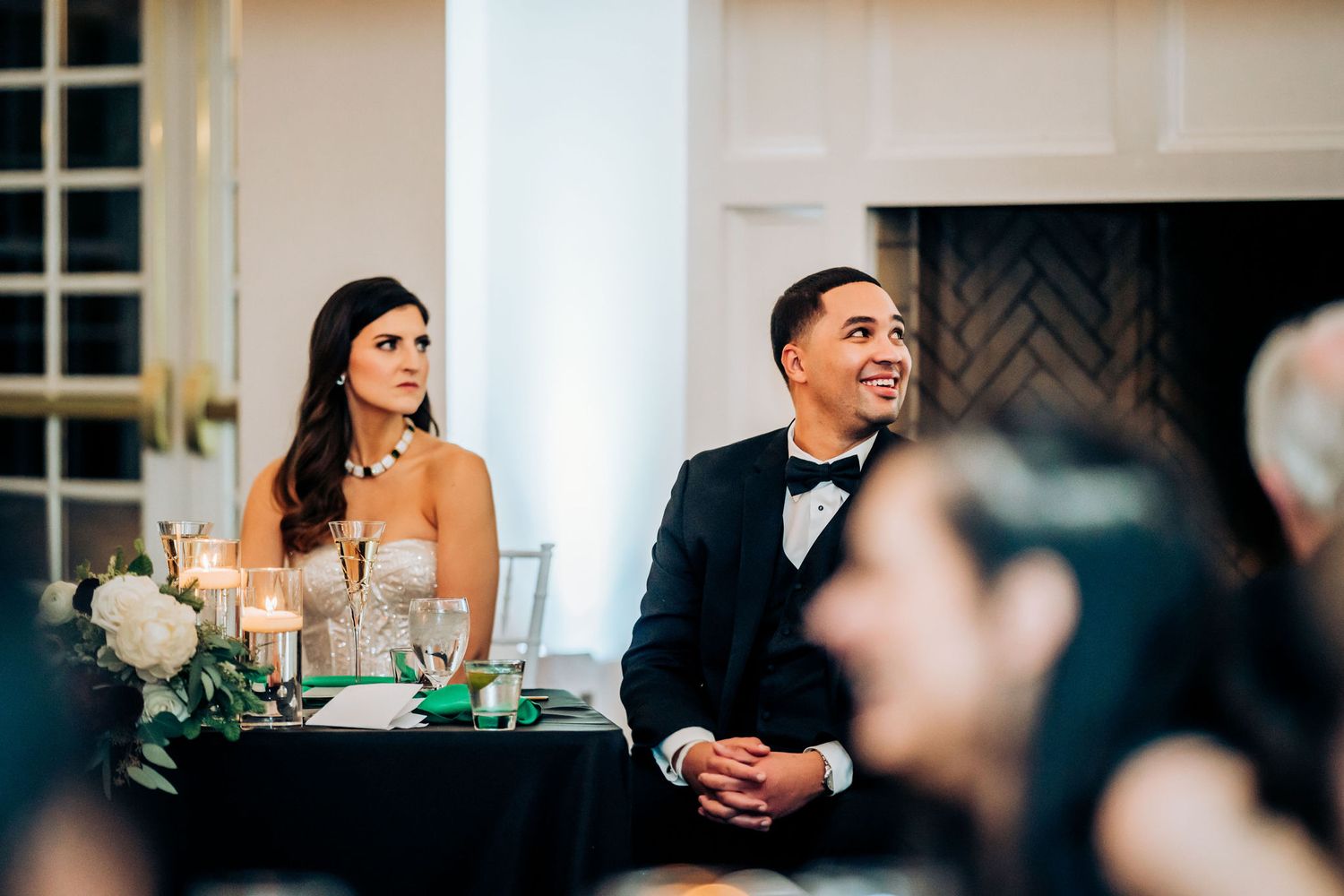 Couple at wedding head table with elegant white floral arrangements and candlelight.