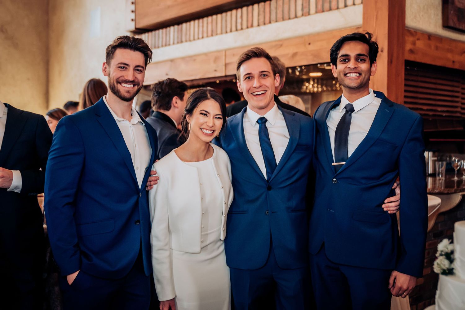 Wedding party poses together in coordinated navy blue suits and white dress for formal portrait.