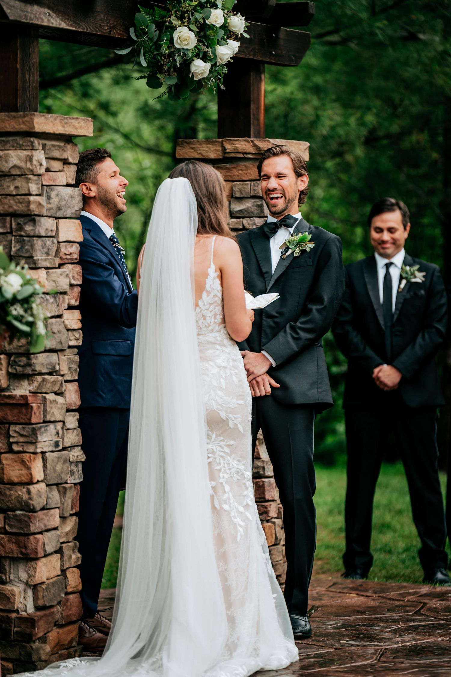 Wedding ceremony moment at rustic outdoor venue with stone pillars and floral decorations.