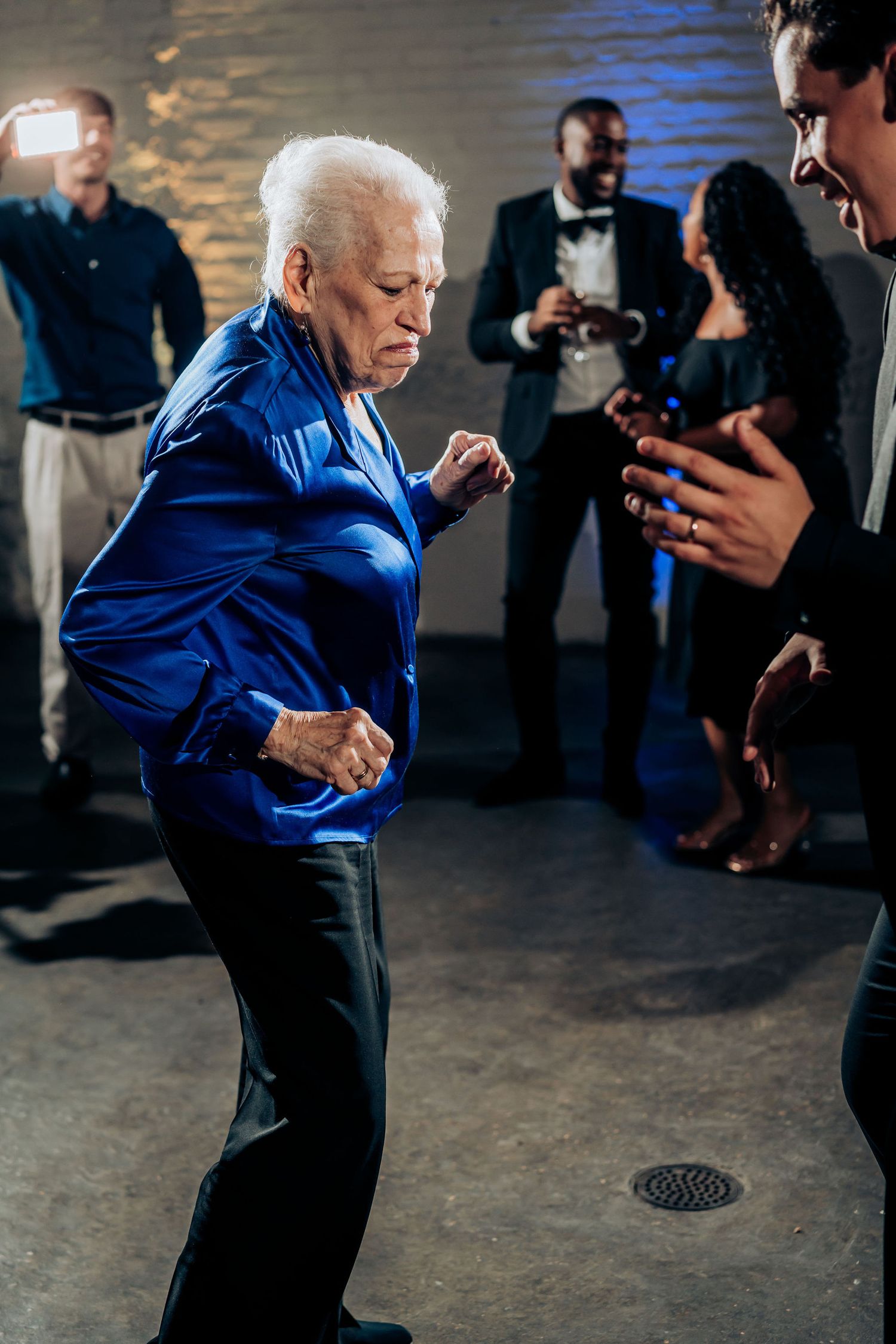 Older guest in bright blue jacket dancing energetically at wedding reception.