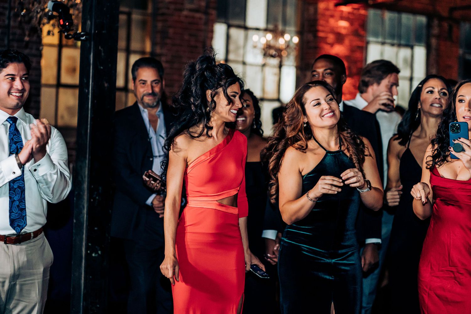 Wedding guests in formal attire enjoying themselves at an elegant brick venue.
