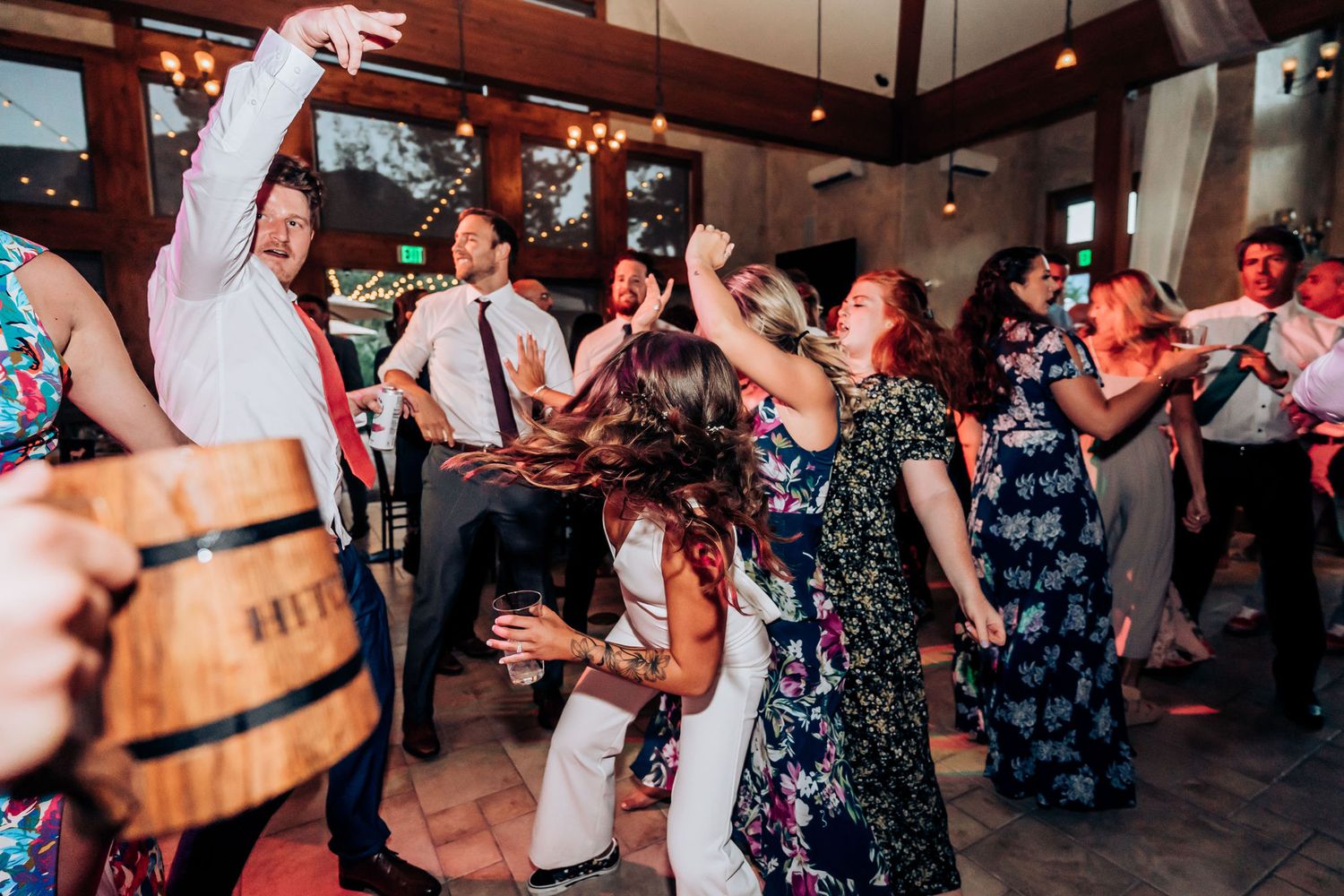 Party guests dancing and having fun at a celebration in a wooden-beamed reception hall.