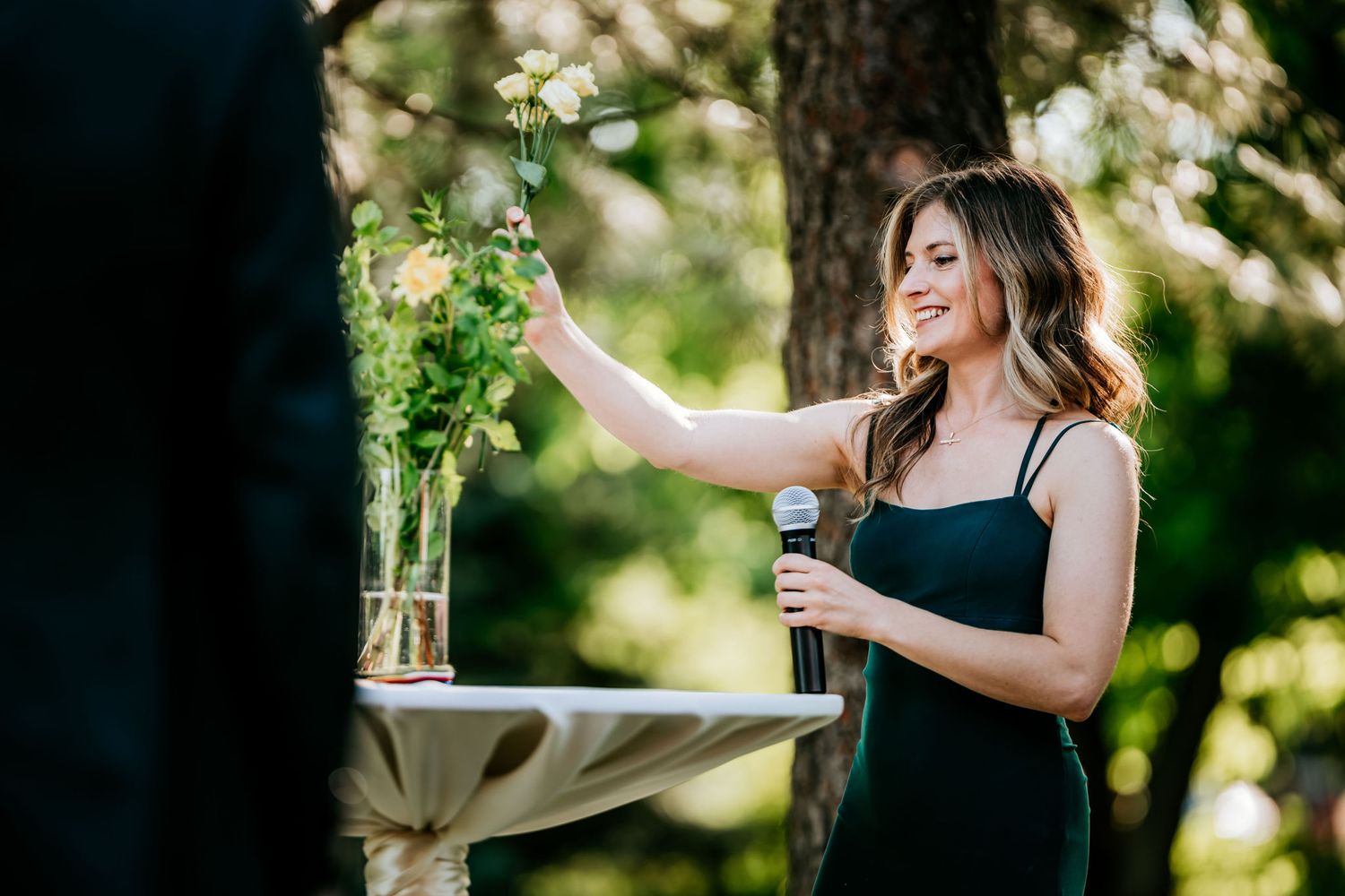 Someone in a black dress arranges flowers in a vase during an outdoor event.