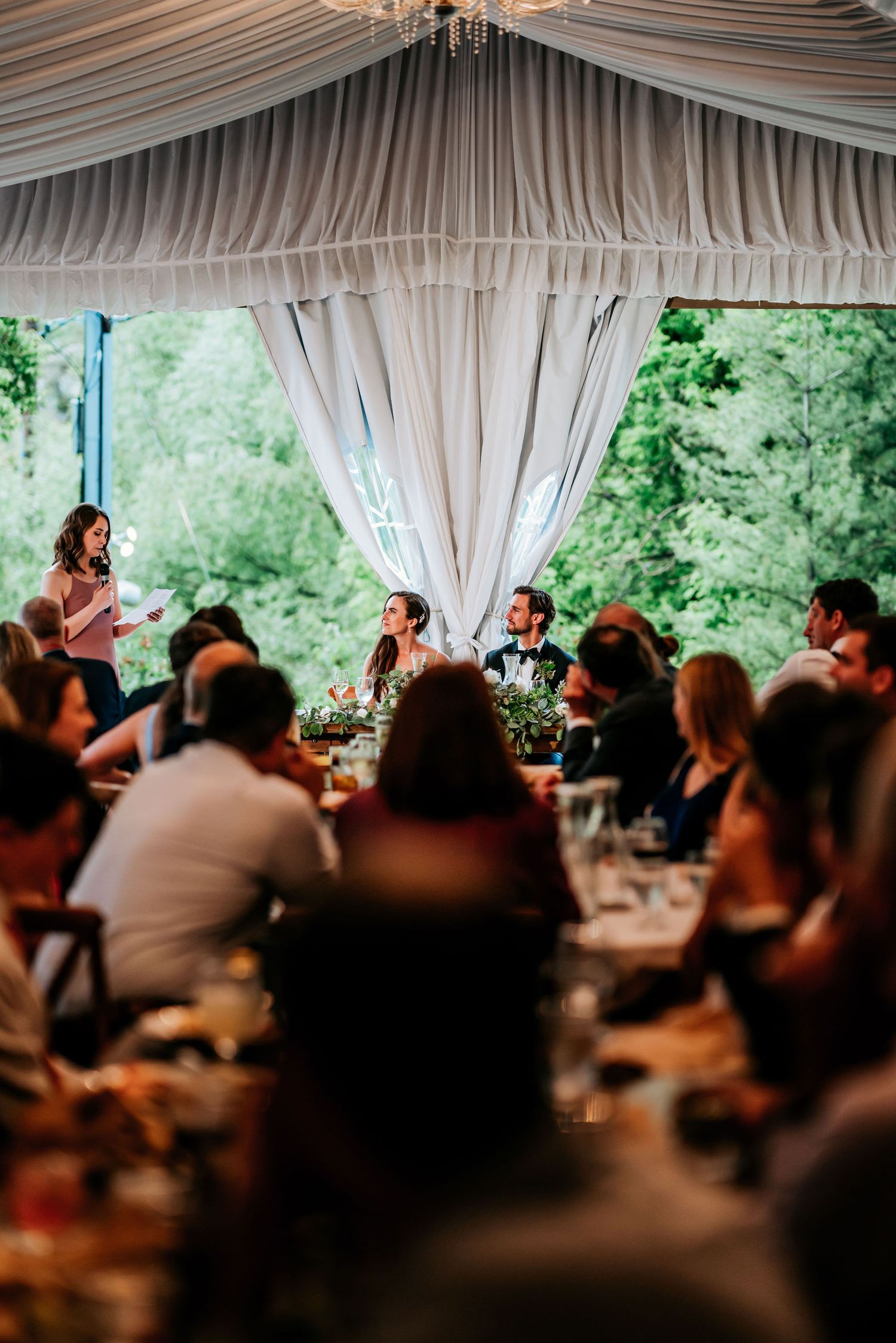 Guests gather under a draped tent canopy for an intimate wedding reception dinner.
